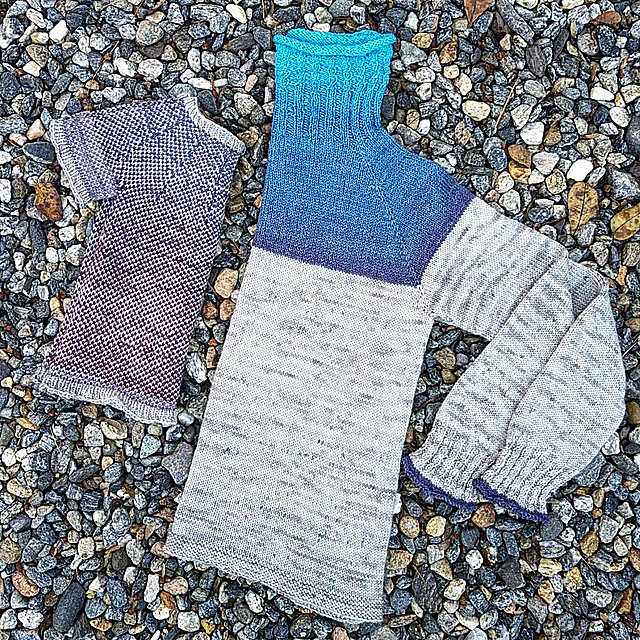 Two sweaters folded in half and placed an inch apart as if to create a complete sweater. The sweater on the left is the sea glass mini, knit using a 1x1 colorwork pattern in a blue to purple gradient with a light gray yarn. The sweater on the right is the Rosemont sweater, knit with a bright to dark blue gradient yoke with the remaining body and sleeves worked in a light gray. The top of the Rosemont yoke to the bottom of the sea glass mini creates a complete blue to purple gradient.